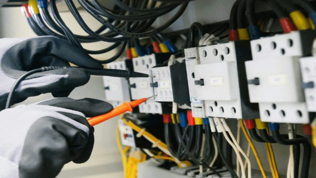 Electrician testing electrical panel with multimeter.